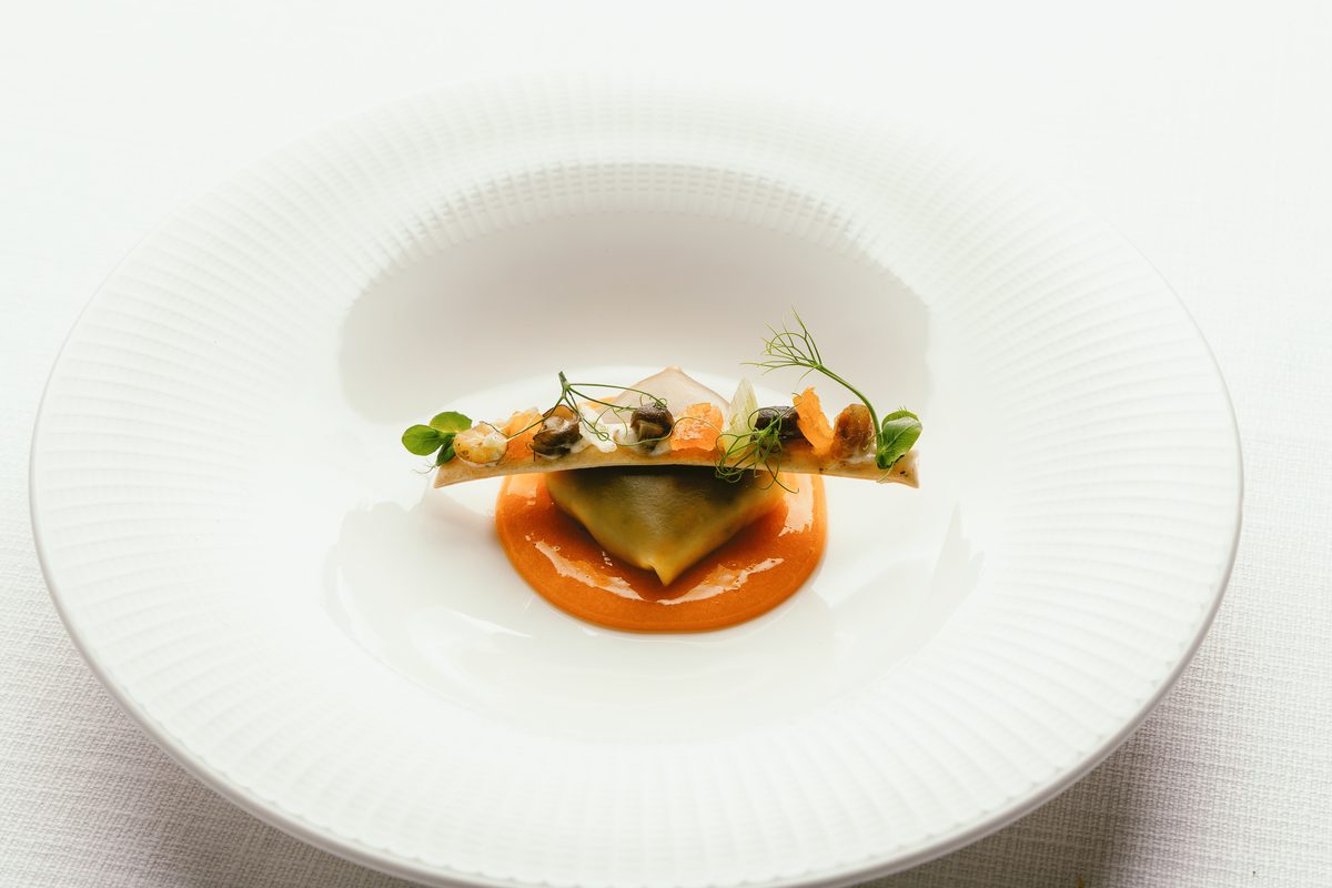 Raviolo con salsa de tomate y brotes, emplatado en la cocina del club